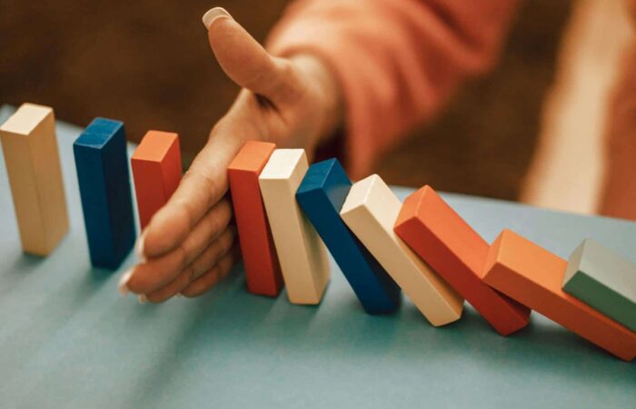 A hand strategically stops falling blue and red domino blocks on a table.
