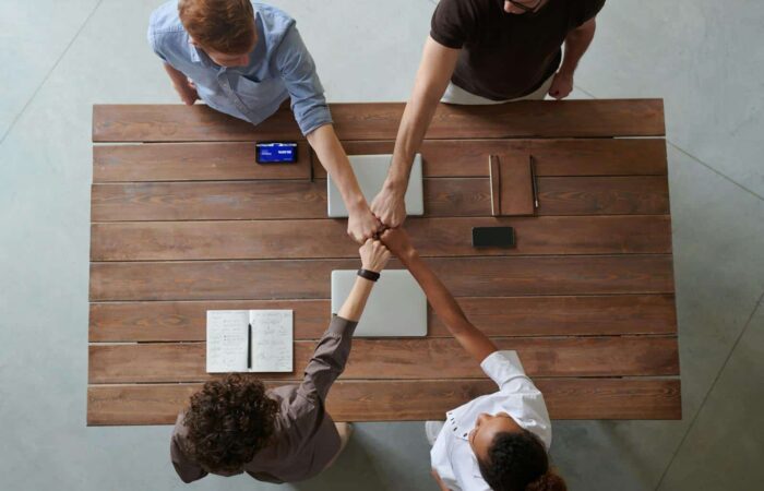 A diverse group of professionals engaging in a teamwork celebration with a fist bump over a wooden table indoors.
