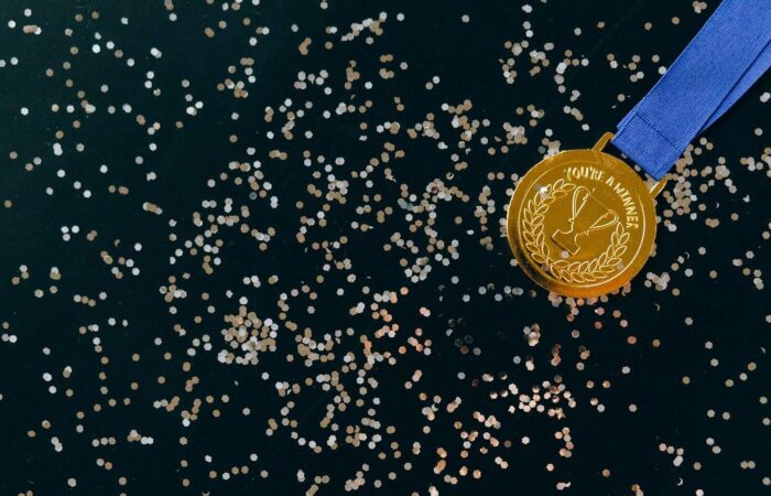 Close-up of a gold medal with blue ribbon and confetti on a black surface, symbolizing victory.
